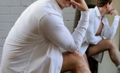 Man in a white shirt poses near a mirror.