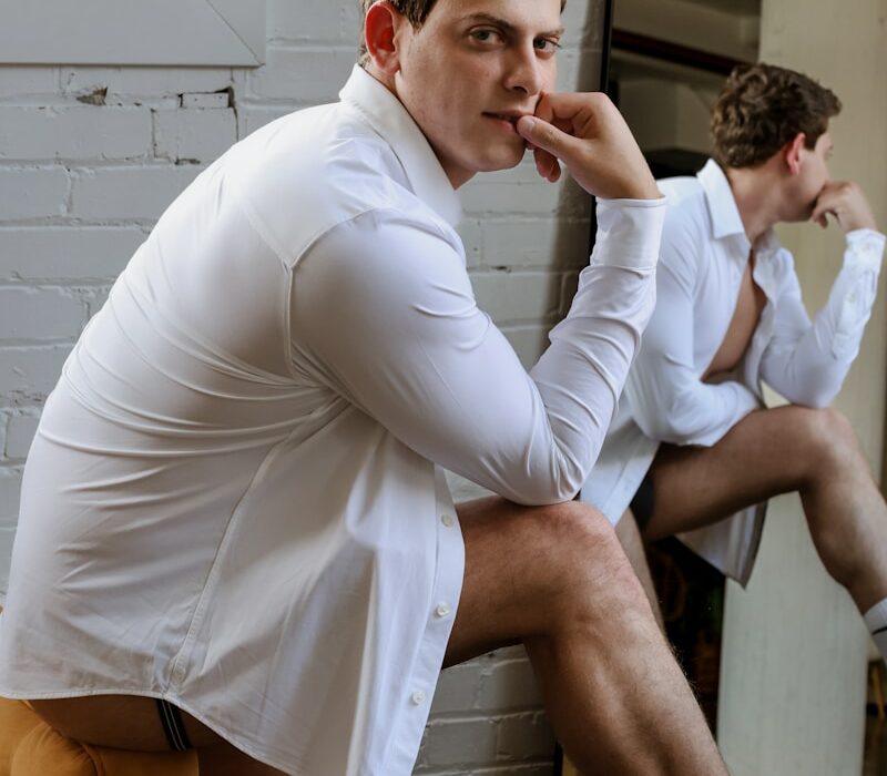 Man in a white shirt poses near a mirror.